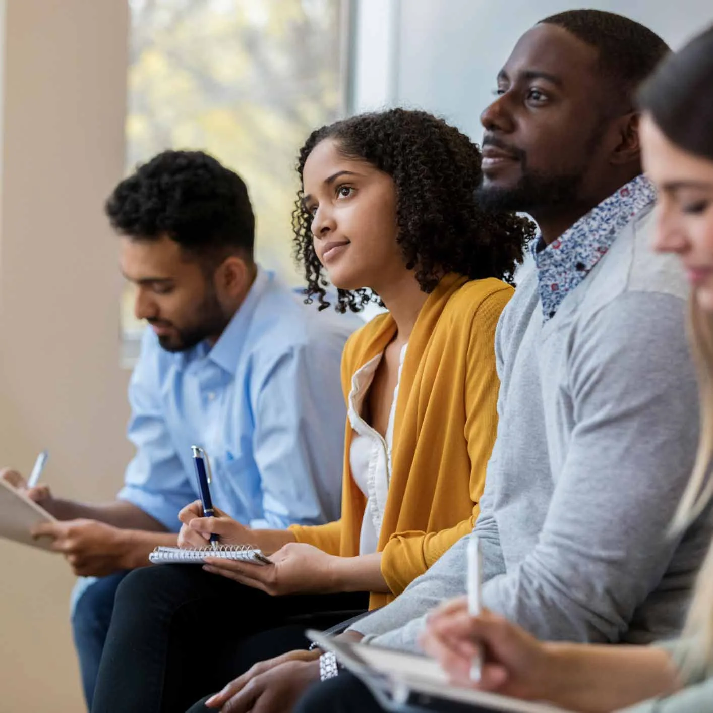 A group of business people sit in a row in a training class. They look at an unseen speaker as they concentrate on his lecture.