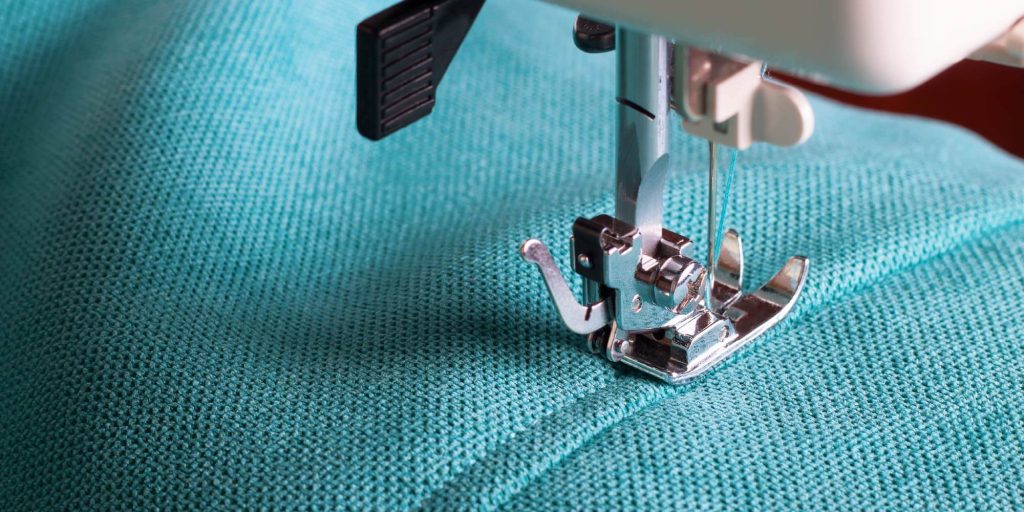 textile worker using sewing machine on turquoise material