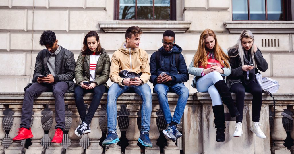 teenagers sitting on wall all checking their phones