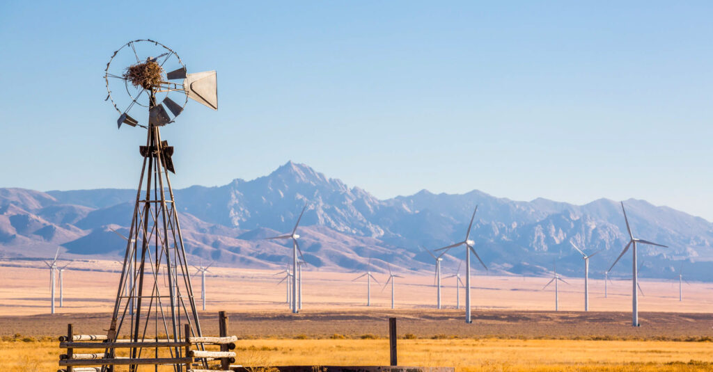 windmill in rural US setting with new windmills and mountains in background