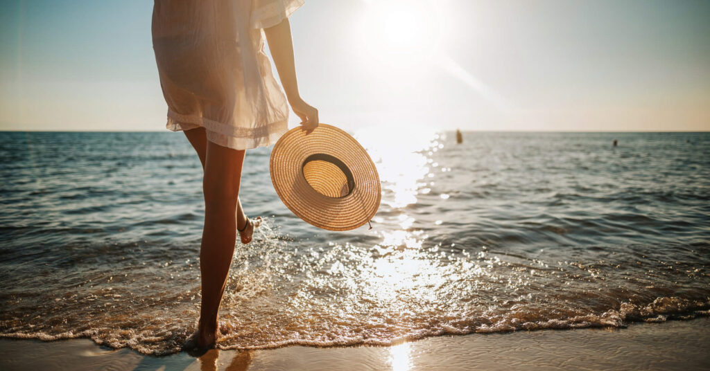 woman on beach at sunset with sunhat in her hand