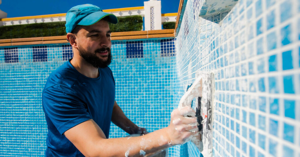 maintenance worker grouting tiles in empty swimming pool under construction