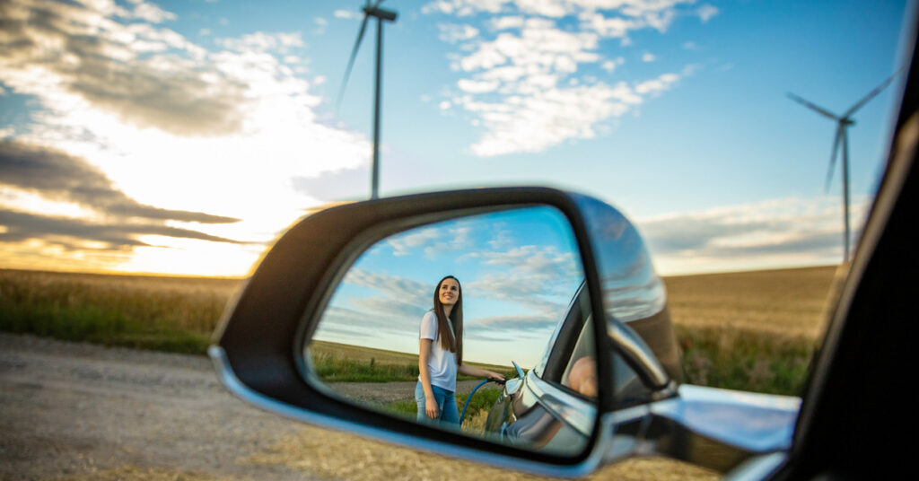 woman charging electric vehicle in front of windmills