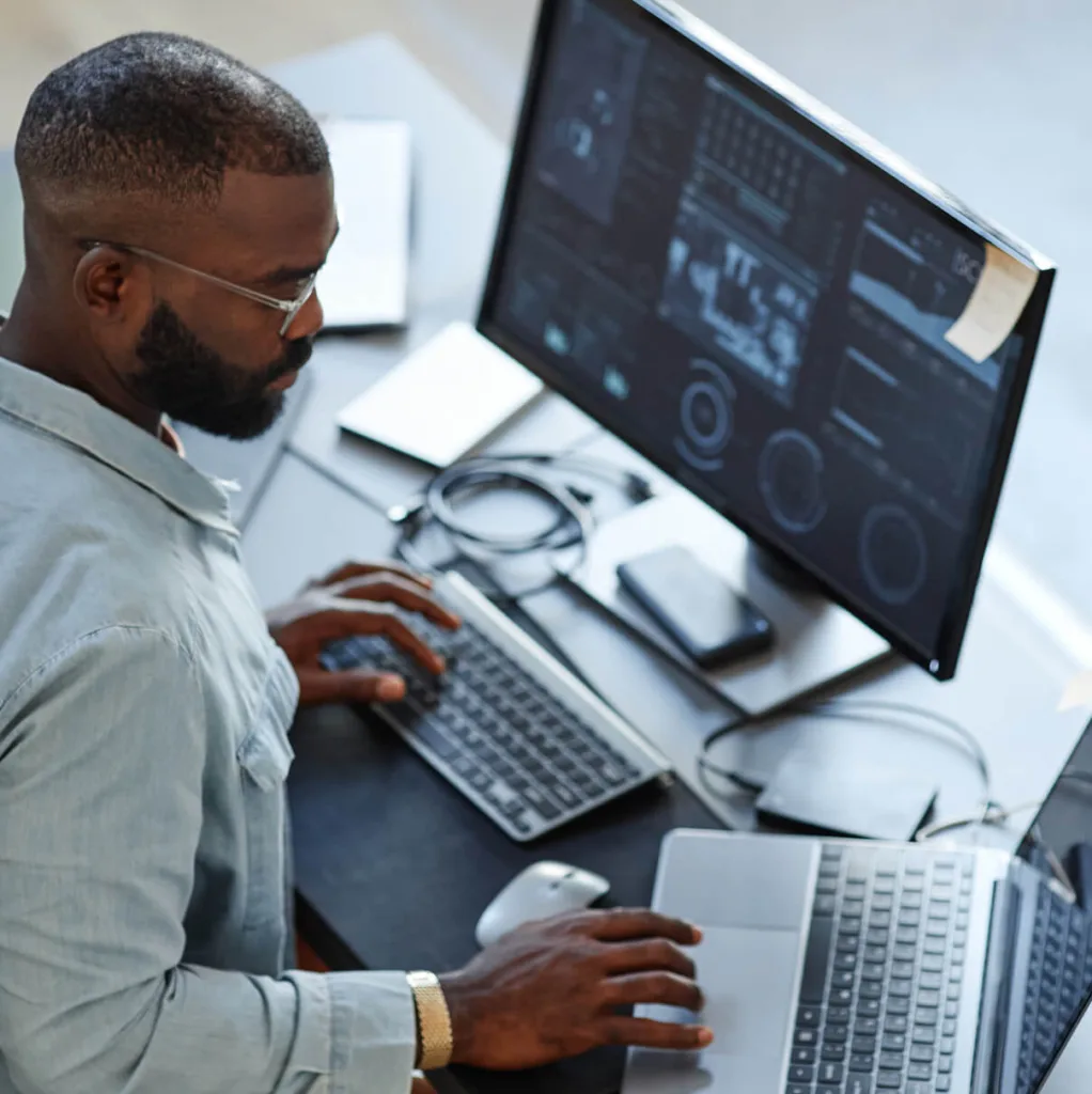 male it worker at desk working on two screens