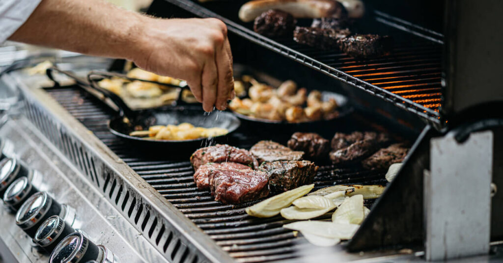 hand seasoning meat on a busy barbecue