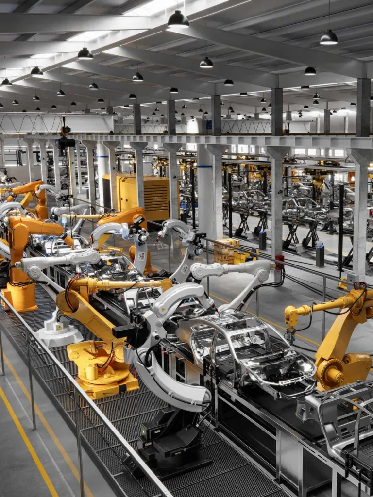 High angle view of cars on production line in factory. Many robottic arms doing welding on car metal body in manufacturing plant.