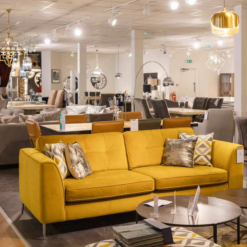 A wide angle of a furniture store with no people in. There is various different sofas and lamps and furniture on the shop floor for display purposes.