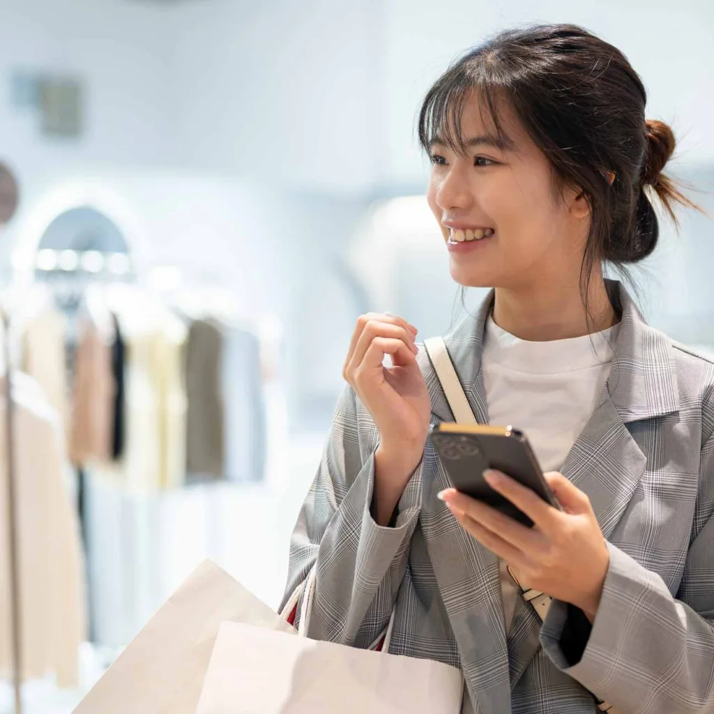 An attractive young Asian woman in trendy clothes with shopping bags is enjoying shopping in a shopping mall.